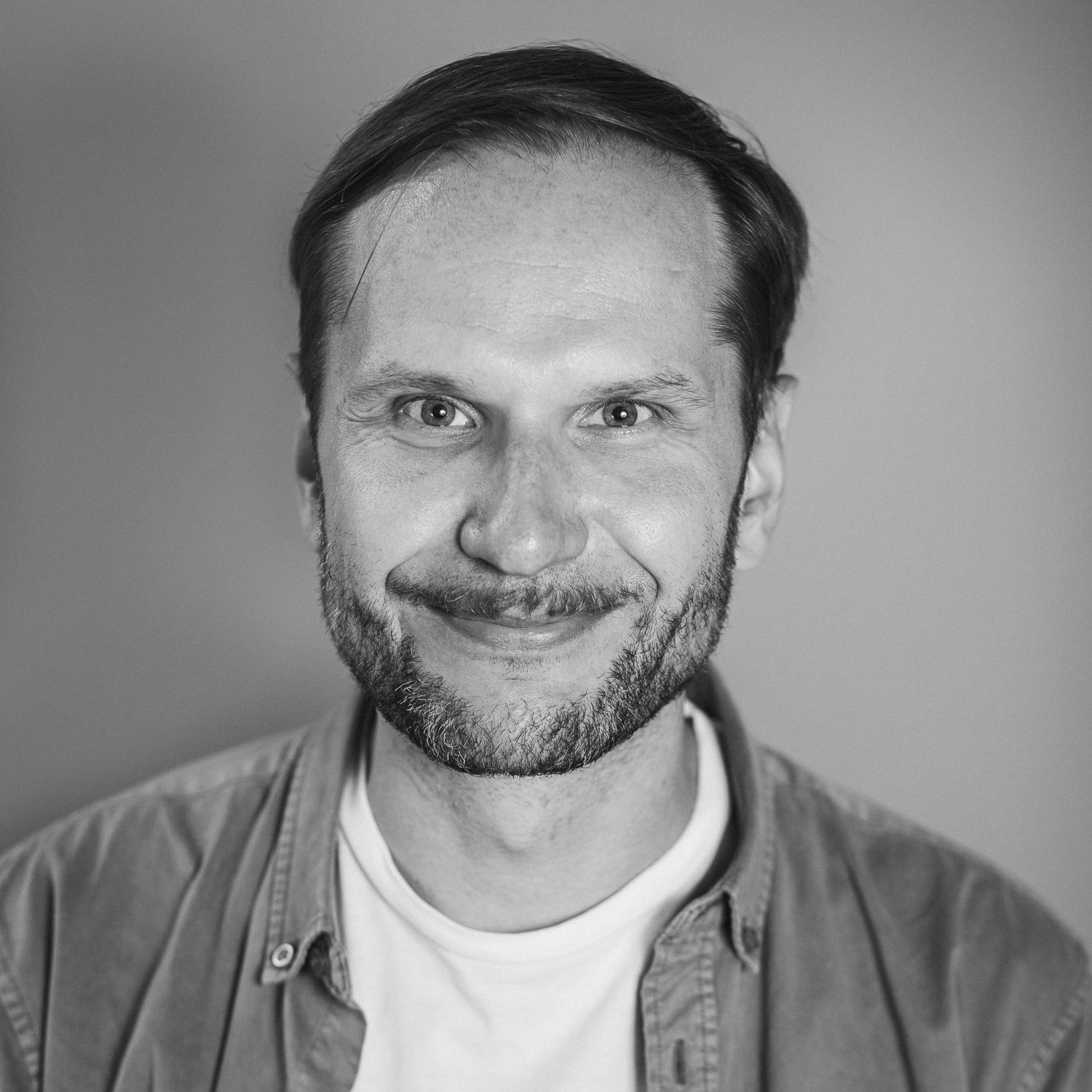 Portraitfotografie eines lächelnden  Mannes Mitte 40 mit Bart und leicht längeren Haaren die zur Seite fallen