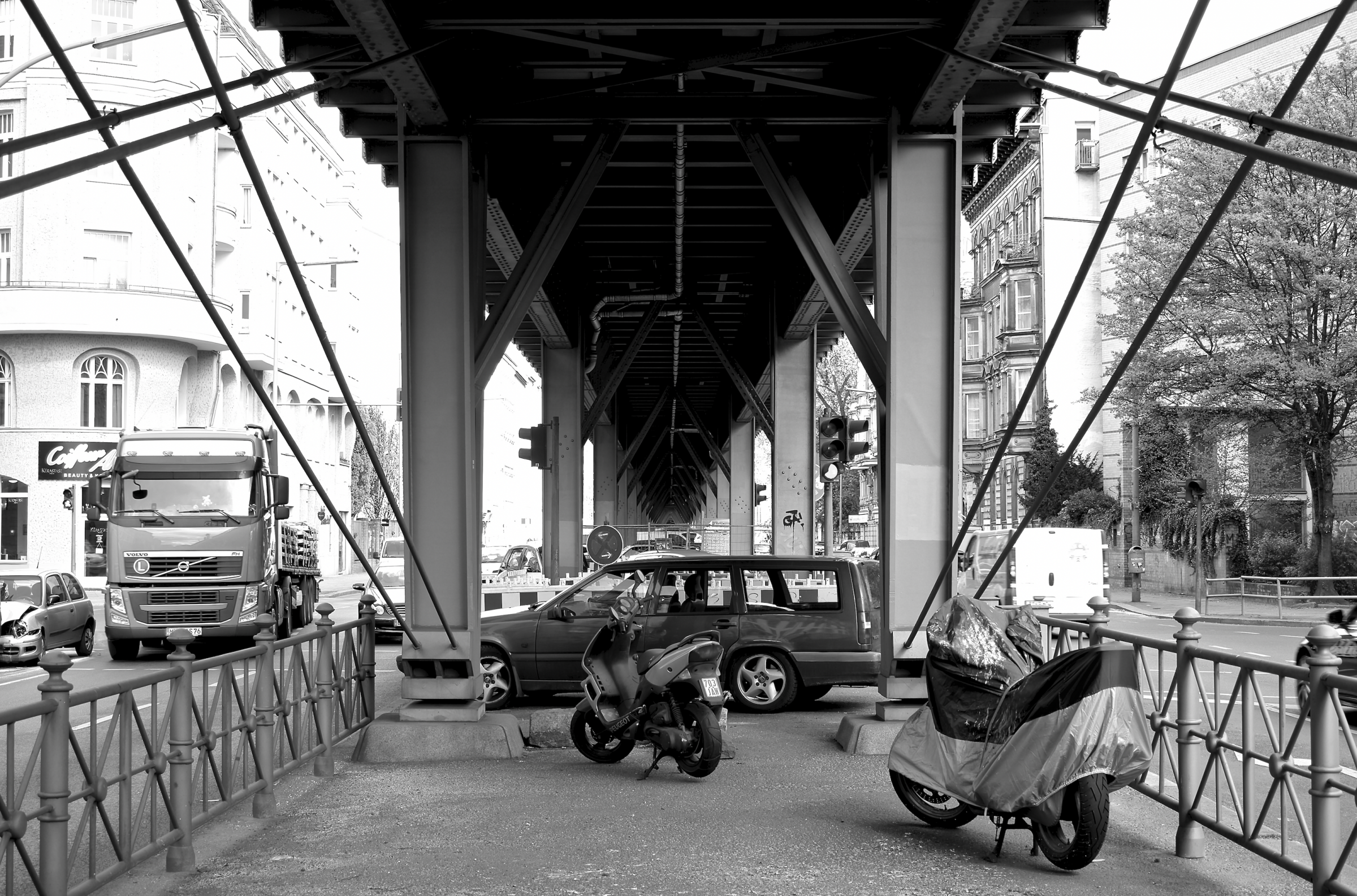 Blick unter das U-Bahn-Viadukt, das mit Autos und Motorrädern zugestellt ist. Daneben die Fahrspuren, auf denen Lastwägen und PKWs unterwegs sind.