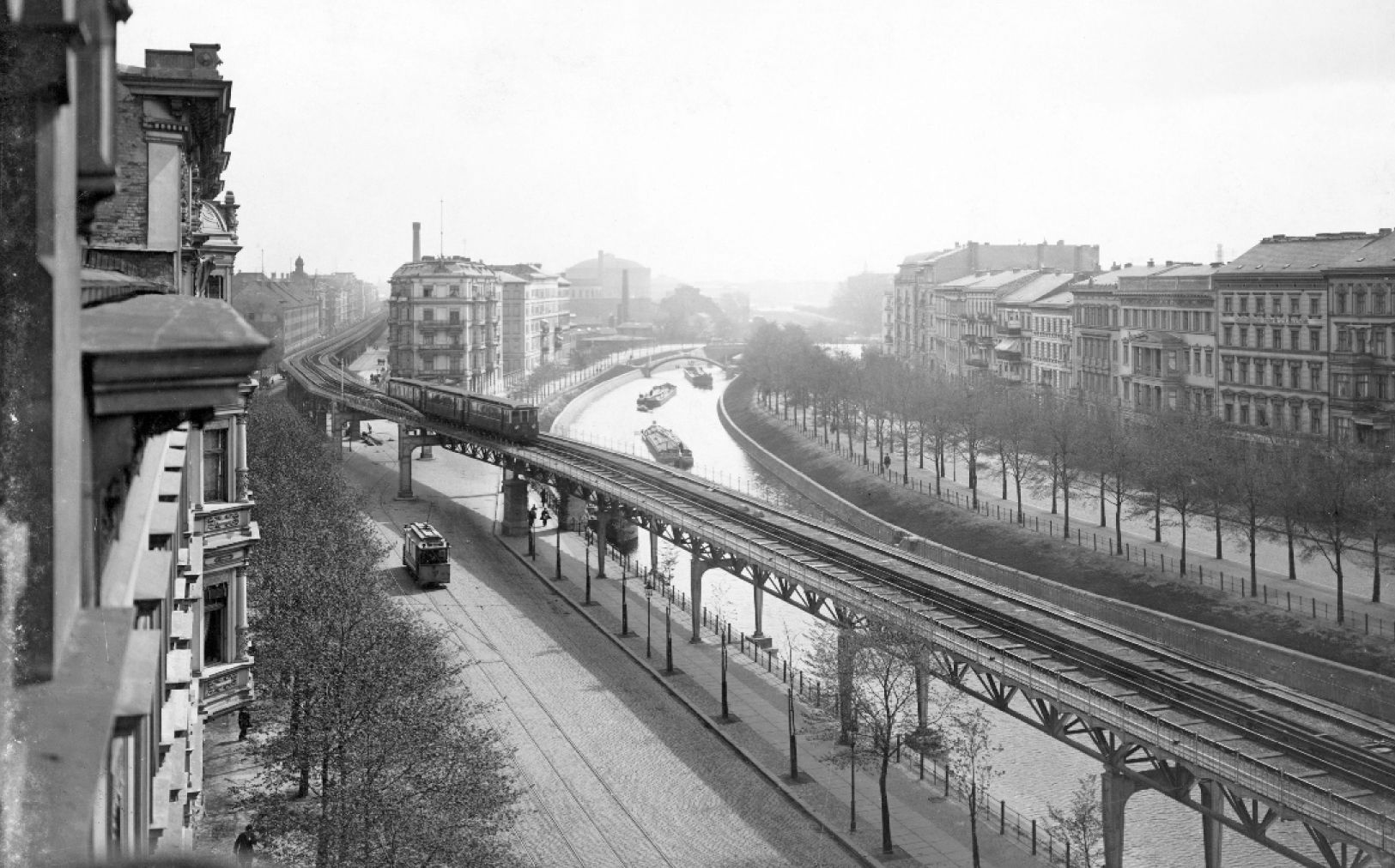 Historisches Foto aus dem 19. Jahrundert. Bick aus einem Fenster auf das Hochbahn-Viadukt- im Hintergrund der Kanal und auf der gegenüberliegenden Seite eine Häuserzeile and typischen berliner Mietshäusern