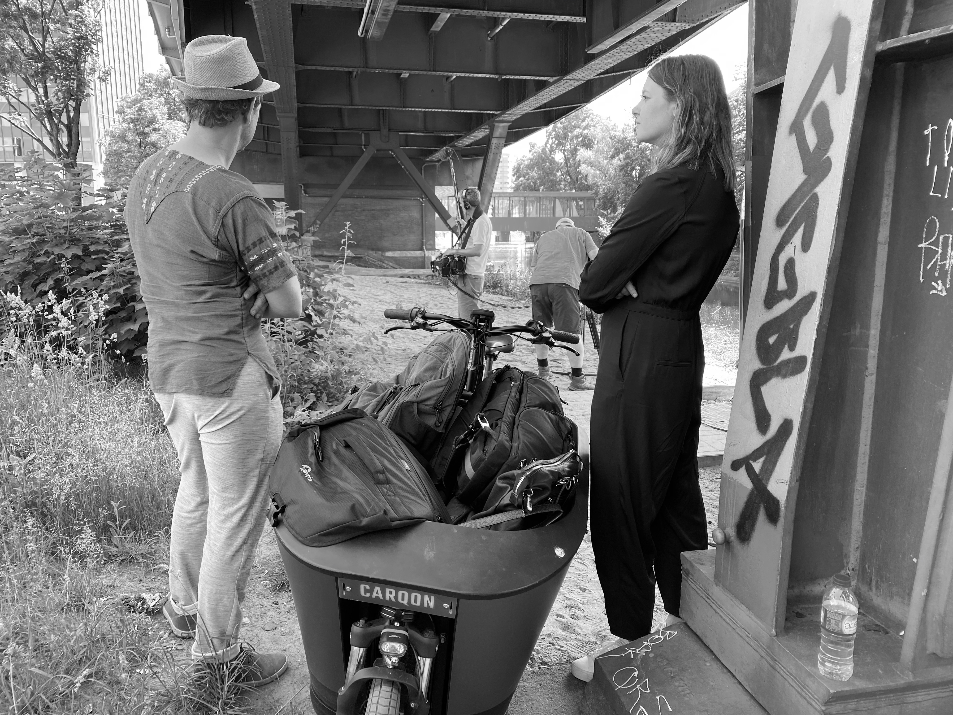 Zwei Menschen stehen unter dem Viadukt auf Höhe der Möckernbrücke neben einem Lastenrad und gucken zu zwei Männern im Hintergrund des Bildes, die mit Dreharbeiten beschäftigt sind.