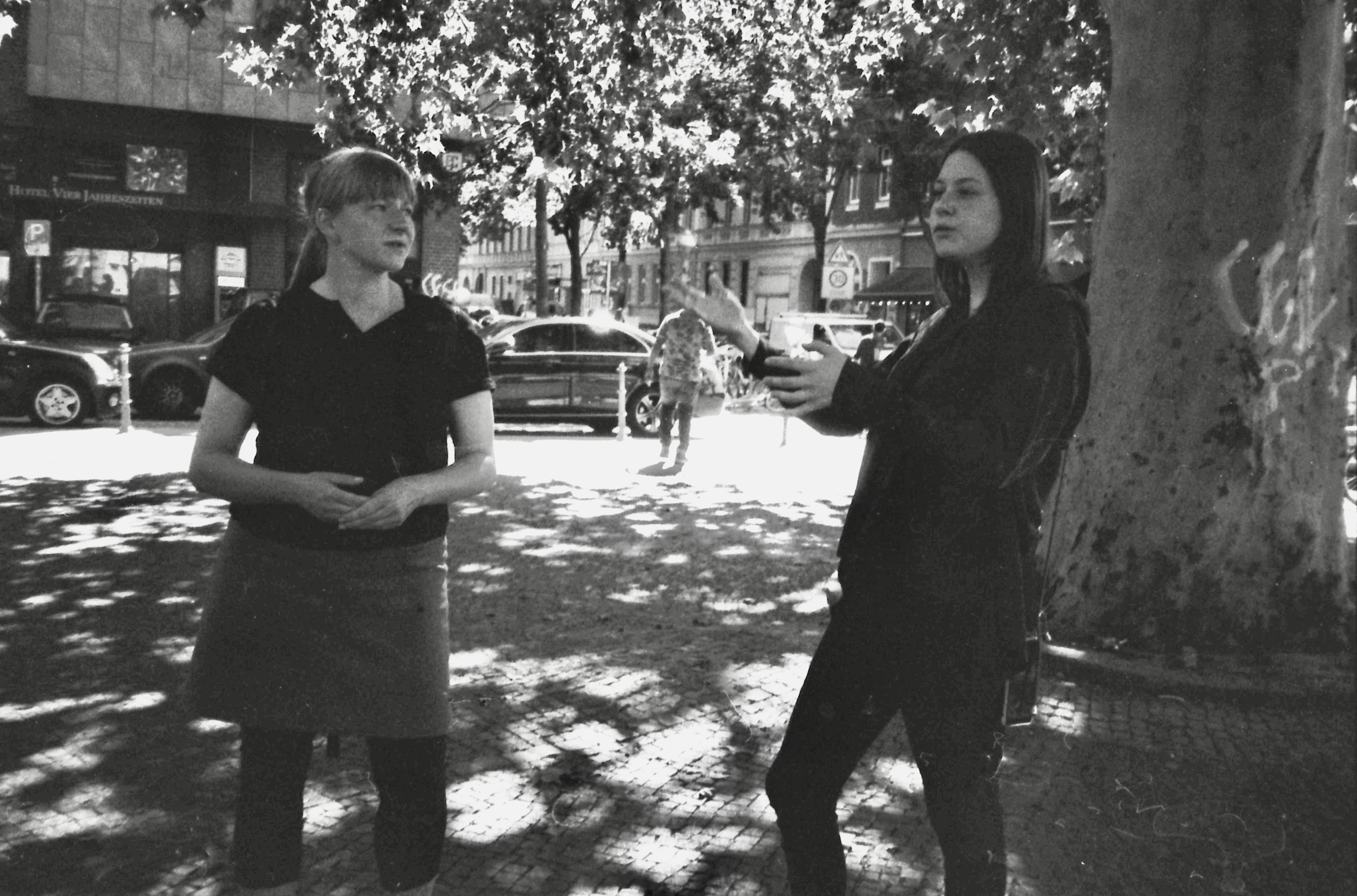 Zwei Frauen stehen an einem Platz in Kreuzberg. Eine der beiden redet und gestikuliert mit den Händen, sie erklärt etwas. Die Andere blickt sie an und hört ihr zu.