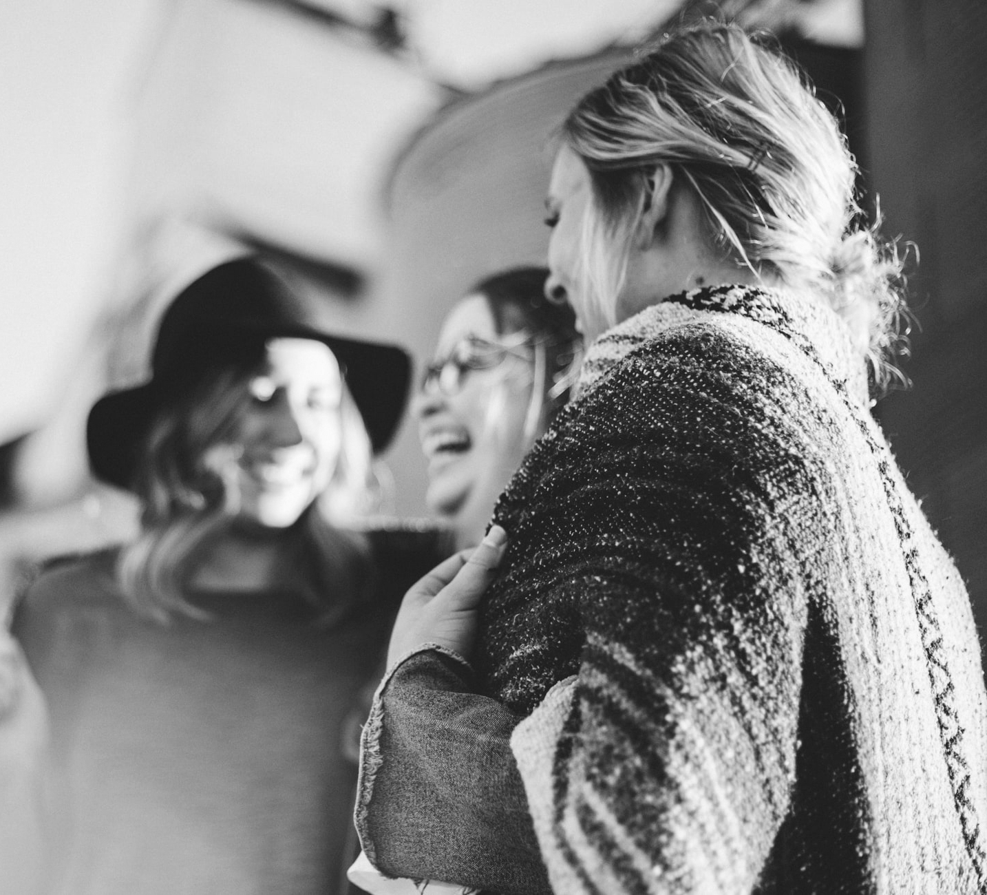 Unscharfe Fotografie, die drei junge Frauen zeigt, die im Gespräch sind und lachen.