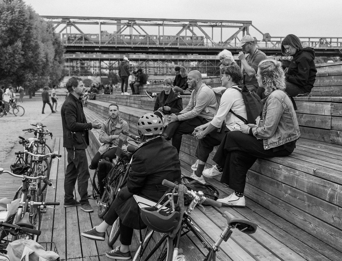 Zehn Personen sitzen verteilt auf drei Stufen im Gleisdreieckpark und höhren einem Sprecher zu. Ihre Fahrräder lehnen an der untersten Stufe.