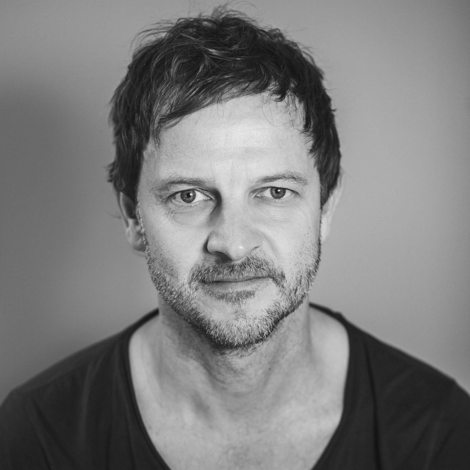 Portraitfogorafie eines Mannes Anfang 50 mit zerzaustem Kurzhaarschnitt und Dreitagebart, der wach in die Kamera guckt; nicht lächelnd, aber trotzdem freundlich.