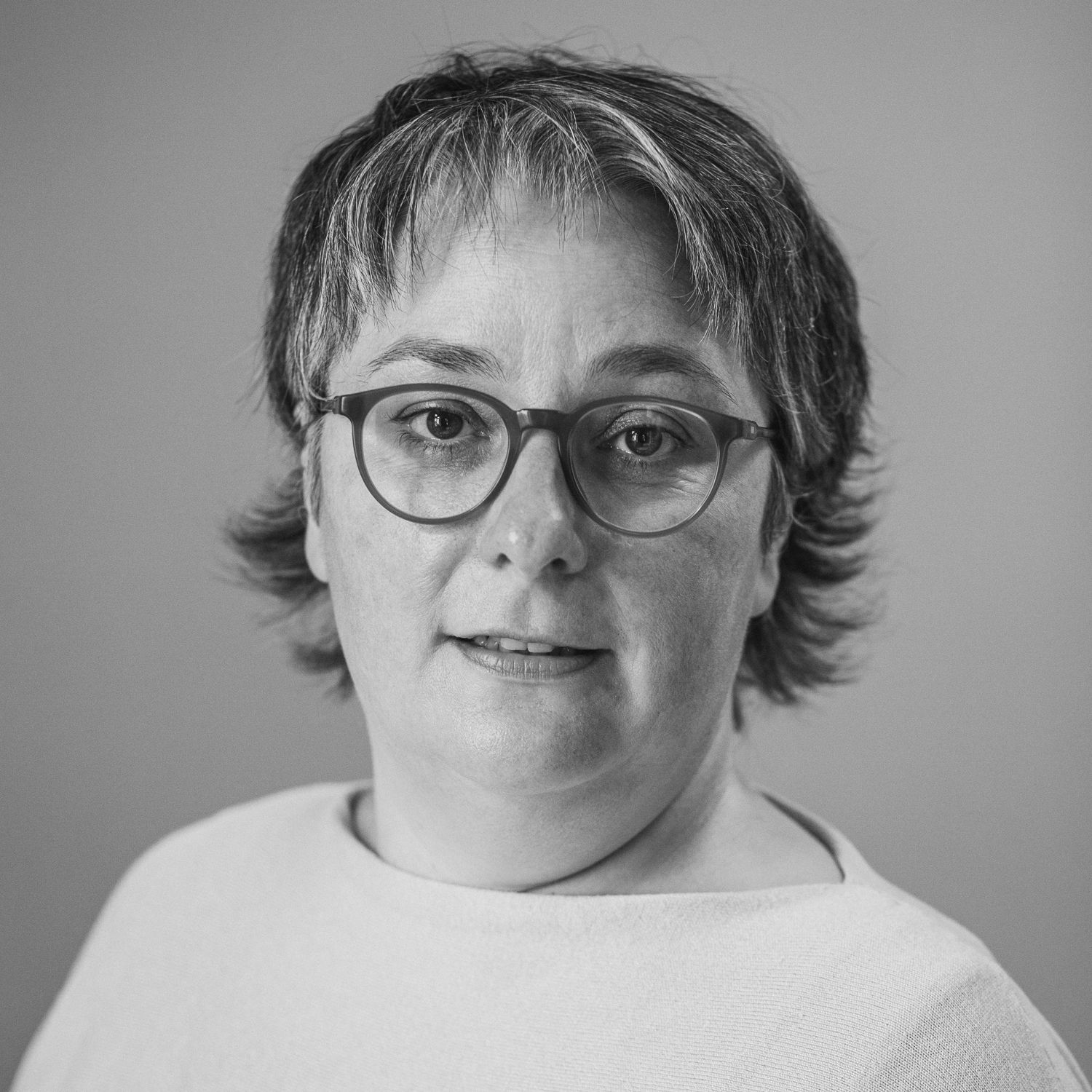 Portraitfotografie einer Frau Mitte 40 mit  Kurzhaarschnitt, die Brille trägt und mit wachen Augen leicht seitlich in die Kamera blickt.