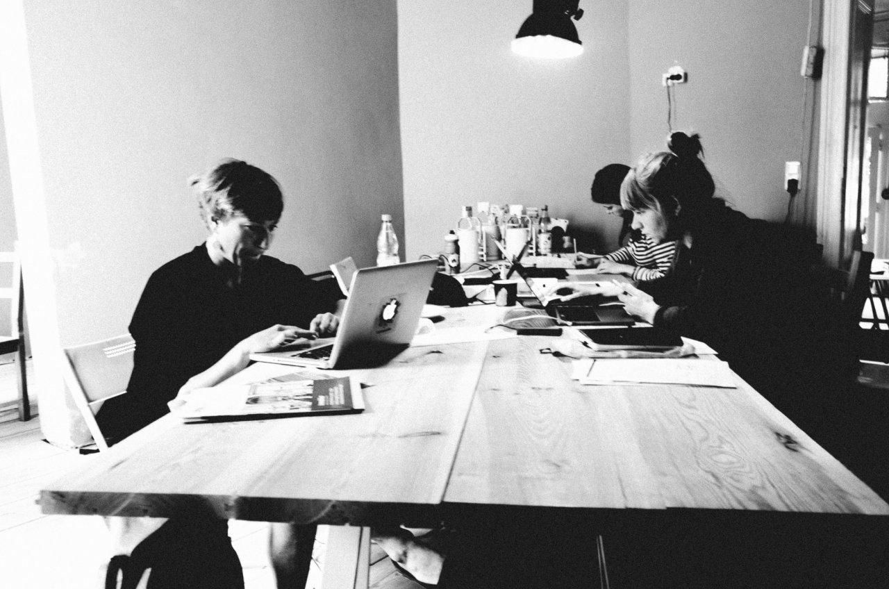 Aufnahme von drei Frauen, die an einem langen Tisch sitzen und vertieft arbeiten.